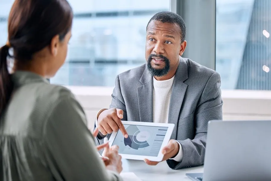 A business professional discussing marketing research data on a tablet with a client.